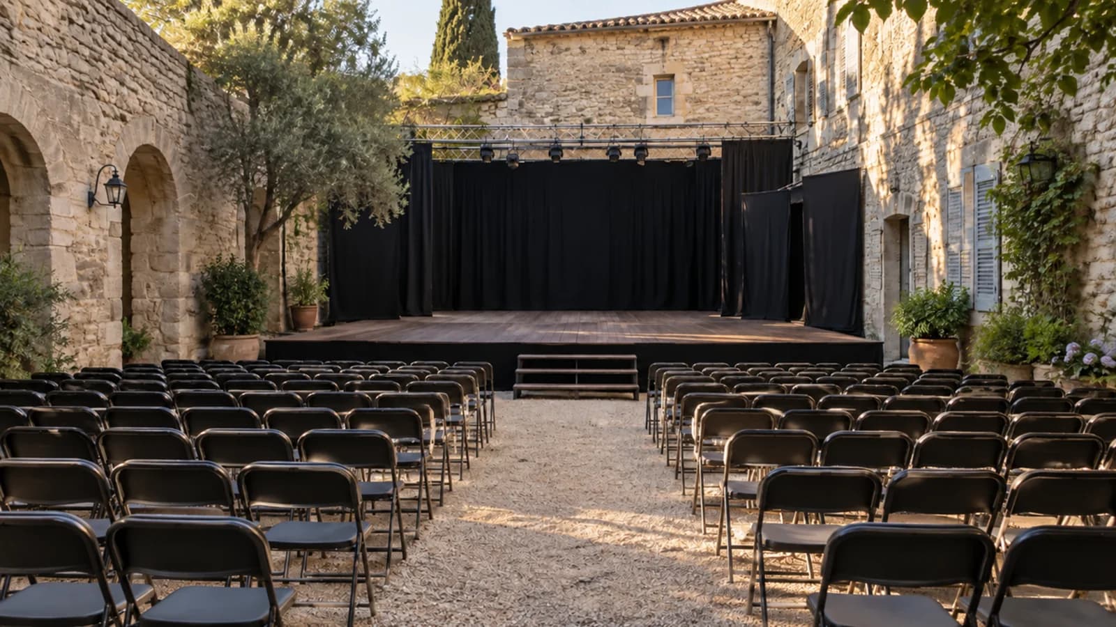 Une petite scène et des rangées de chaises dans une cour de pierre fictive.
